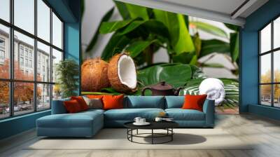 Two tropical coconuts lying near a teapot and two cups for spa therapy among greenery Wall mural