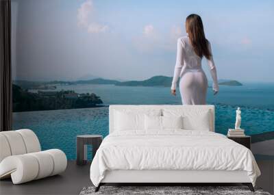 view from behind on fit woman with long brown hair in a long white tight  dress looking on the infinity pool and beautiful sea. Summer vacation Wall mural