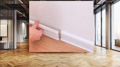 A man installs a floor skirting board. Fixing the plastic skirting board with screws to the wall. Home renovation. Wall mural