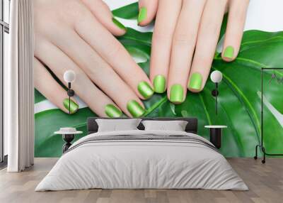 Female hand with 2 different glitter nail polishes. Green nail design with 2 shades. Women hand with sparkle manicure and green plant on background Wall mural