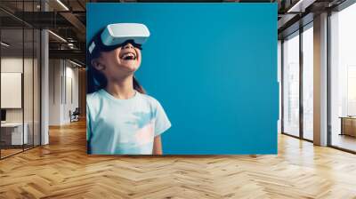 Young girl getting experience using VR headset glasses isolated on a blue background with copy space Wall mural