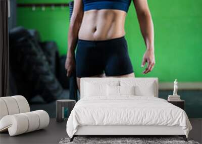 Female fitness model doing cross fit exercise in a gym with a sledge hammer Wall mural