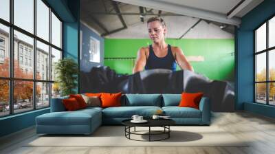 Female fitness model doing cross fit exercise with a massive tyre in a gym Wall mural