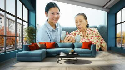 Asian elder woman doing a physical therapy exercise with her granddaughter by using dumbbells. Wall mural