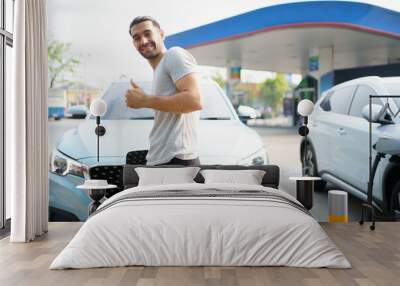 Handsome Asian young man holding an EV plug connector and attaching onto the car. Wall mural