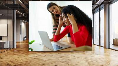 Unhappy - worried young woman expressing an unwell face in front of the notebook computer and her friend come to encourage her. Wall mural