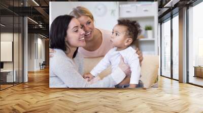 Female couple sitting in their home, playing with their baby son. Wall mural