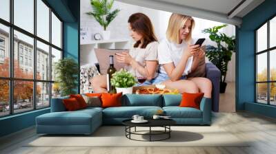 internet addiction concept - two young female friends eating pizza, drinking wine and browsing in their smartphones in cozy living room Wall mural