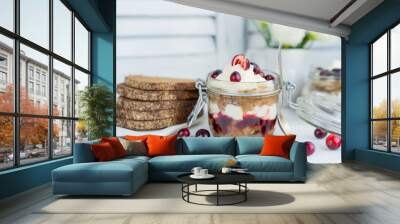 Latvian, scandinavian traditional rye whole grain bread layered dessert with whipped cream and cowberry jam served in glass jar on a white table with flowers and berries, copy space. Wall mural