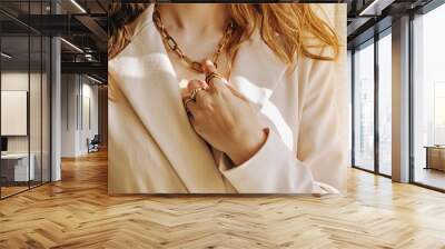 Close-up of female hand with rings touching her golden chain necklace, natural light Wall mural