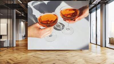 Close up view of man and woman hands holding glasses with cocktail of orange color Wall mural