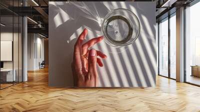 Female hand touching a glass of clear water, view from the top, white table, morning light Wall mural