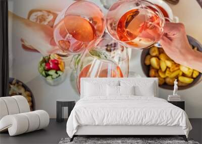 Hands holding glasses with rose wine over the table with food. Wall mural