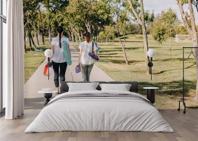 Two young women walking in the morning park, going to do yoga outdoors Wall mural