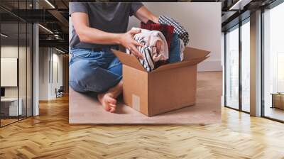 Unrecognizable woman putting clothes in cardboard box while sitting on the floor. Wall mural