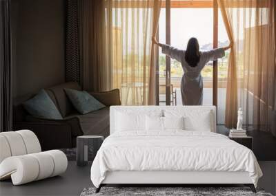 Woman opening curtains in hotel room in the morning Wall mural