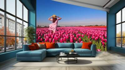 Woman tourist in pink dress and straw hat standing in tulip field Wall mural