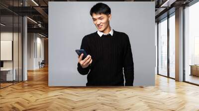 Chinese young man using the cellphone isolated on gray background Wall mural