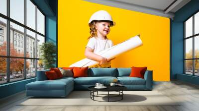 Cute little girl engineer with helmet holding bluepring on yellow background Wall mural