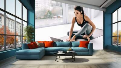 Fit young woman watching online tutorials on laptop, training in living room Wall mural