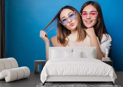 Friends forever. Two cute lovely girl friends in sunglasses posing with smile isolated on blue background Wall mural