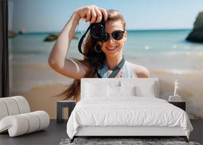 Happy woman on vacation photographing with a camera on the beach and smiling Wall mural