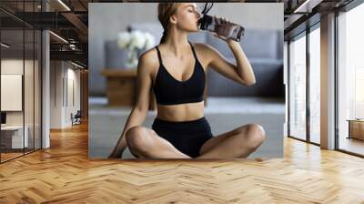 Keep hydrated. Young fit woman drinking water on yoga mat at home Wall mural