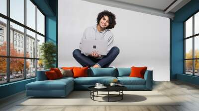 Portrait of a happy curly man sitting on the floor with laptop computer isolated on a white background Wall mural