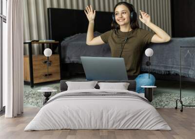 Portrait of a smiling young woman listening to music with headphones and using laptop computer while leaning on a couch at home Wall mural