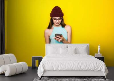 Portrait of confused woman with mobile phone on the yellow background Wall mural