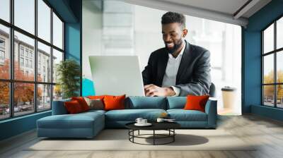 Thoughtful African American businessman using laptop, pondering project, business strategy, puzzled employee executive looking at laptop screen, reading email, making decision at office Wall mural