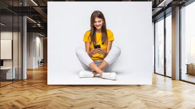 Woman sitting on floor and text messaging on a mobile phone isolated over white background Wall mural