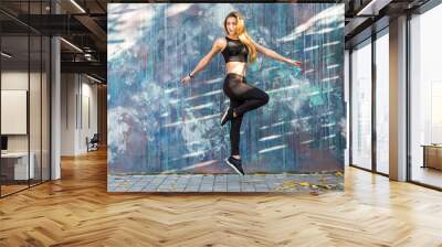 Young fitness woman in sportwear jump in front of street wall background. Outdoors Wall mural