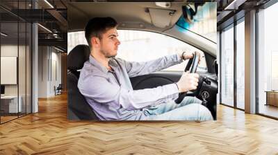 Young man sits in a newly bought car holding his hands on a rudder Wall mural