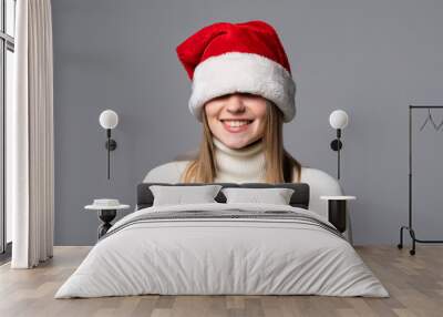 Young woman covering her eyes with santa hat on grey background Wall mural