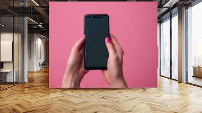 Young adult woman hand holding smartphone and touching black screen with finger on light pink table background. Pastel color. Empty place for text. Wall mural