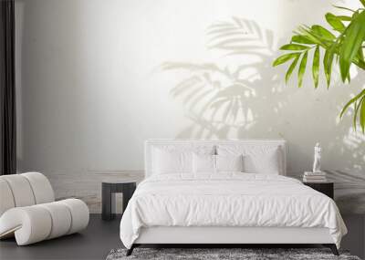 Blank wooden table space with green houseplant leaves in sunlight shadow on abstract stucco wall background Wall mural