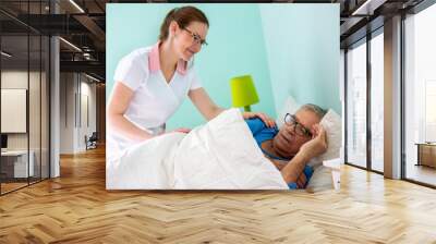 Elder man resident of a nursing home sleeping while medical staff nurse is covering him with sheet Wall mural