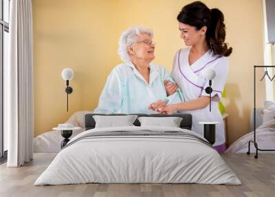 two women teamwork, lady doctor holding senior woman resident by her arm helping her Wall mural