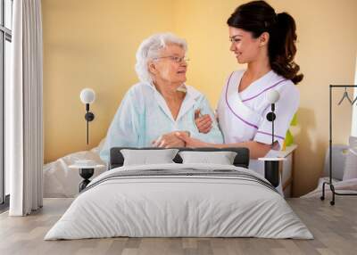 Two women teamwork, lady doctor holding senior woman resident by her arm helping her Wall mural