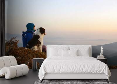 young woman and dog admiring sunrise high in the mountain Wall mural