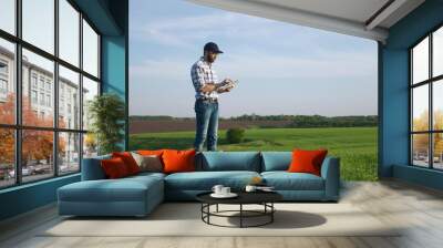 Farmer with a beard and a cap works on the field in spring, use a digital tablet. Farmer using digital tablet. Concept of technologies. Wall mural