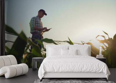 Young farmer working in a cornfield, inspecting and tuning irrigation center pivot sprinkler system on smartphone. Wall mural