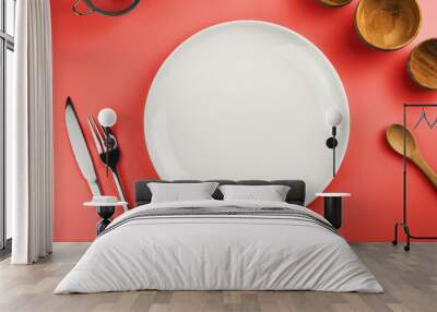 Empty white plate on the red table. Top view. Kitchen utensils beside like fork, knife, bamboo containers Wall mural