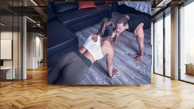 Cheerful couple of two athletic caucasian concentrated guys training push up in living room. Beautiful girl and young man doing push-ups sport routine concentrating on the floor in their studio house Wall mural