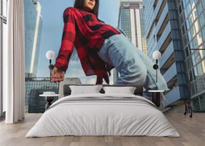 Photo shoot of stylish caucasian hip hop dancer posing on her toes with red shirt, jeans and black boots shoes and top with a urban town as background. City shooting of moving model bending the back Wall mural