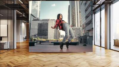 Photo shoot of stylish caucasian hip hop dancer posing on her toes with red shirt, jeans and black boots shoes and top with a urban town as background. City shooting of moving model bending the back Wall mural