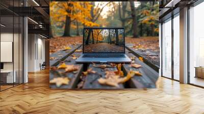 Laptop displaying a forest scene on a picnic table in an autumn park, blending technology and nature. Wall mural