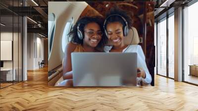 mom and daughter of an African-American woman watch a movie on a laptop while they fly on a trip on a private plane Wall mural