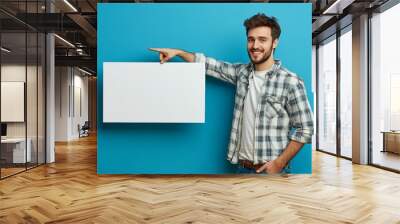 Happy man pointing down at white blank advertising board with empty space for text, blue background, mockup, Generative AI Wall mural